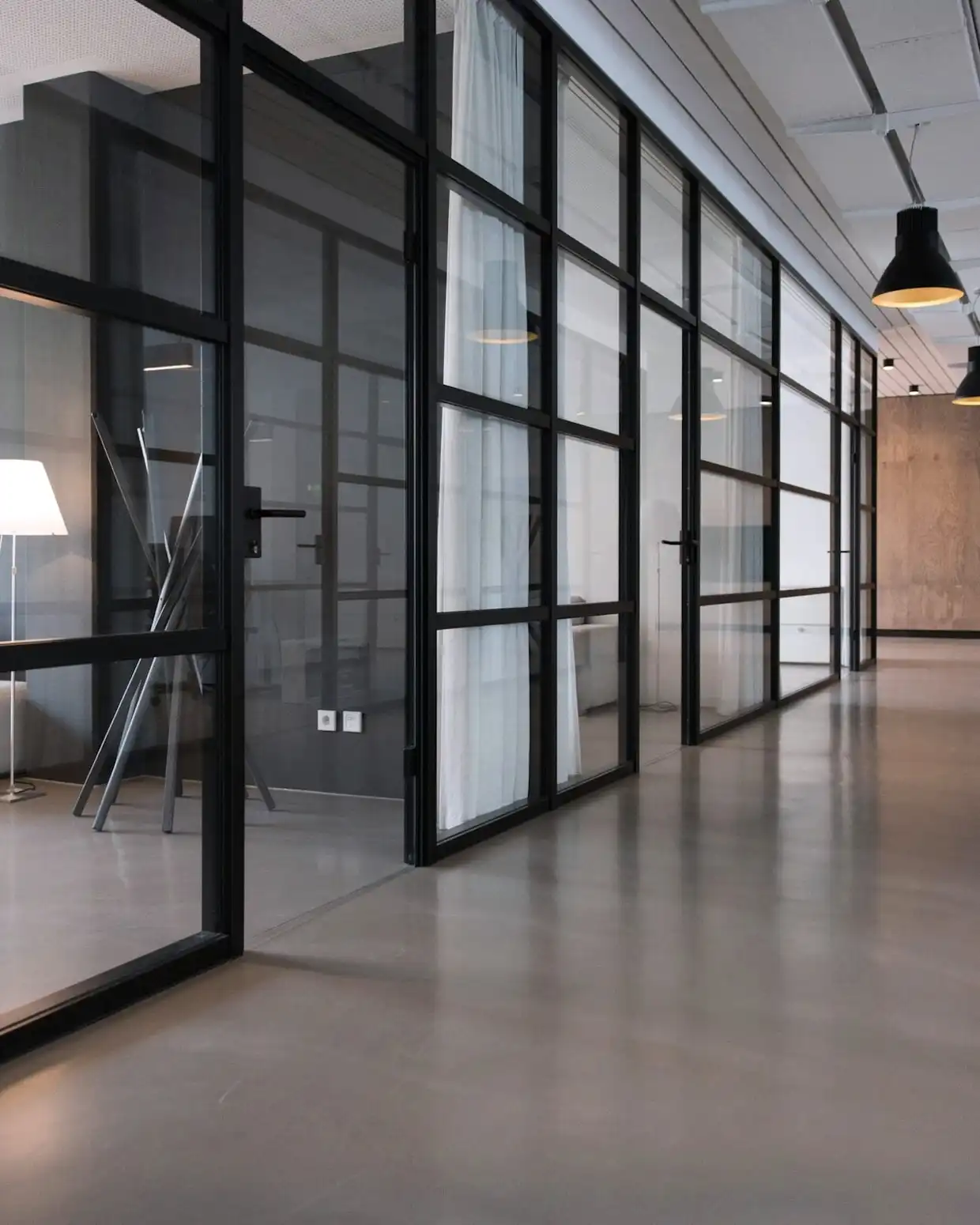 Modern office corridor with black-framed glass meeting rooms and pendant lights